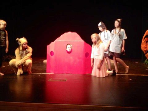 children are standing on a stage with a red structure